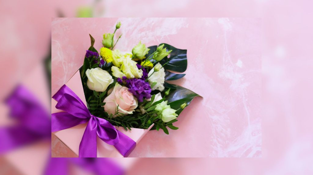 ramo de flores en tonos suaves presentado sobre caja regalo con lazo morado