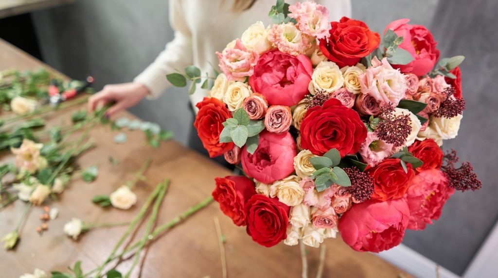 Florista preparando un ramo de rosas rojas y peonías para regalar a la pareja.