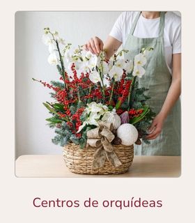 Con flores liofilizadas Florista terminando un centro de orquídeas naturales y elementos liofilizados encima de una mesa de madera clara.